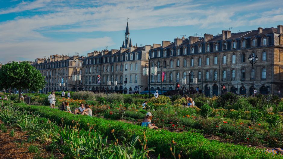A well-maintained urban garden in De Beauvoir Town featuring neatly edged flower beds with a variety of blooming plants and greenery. The garden includes lush grass pathways, mulched soil, and trimmed